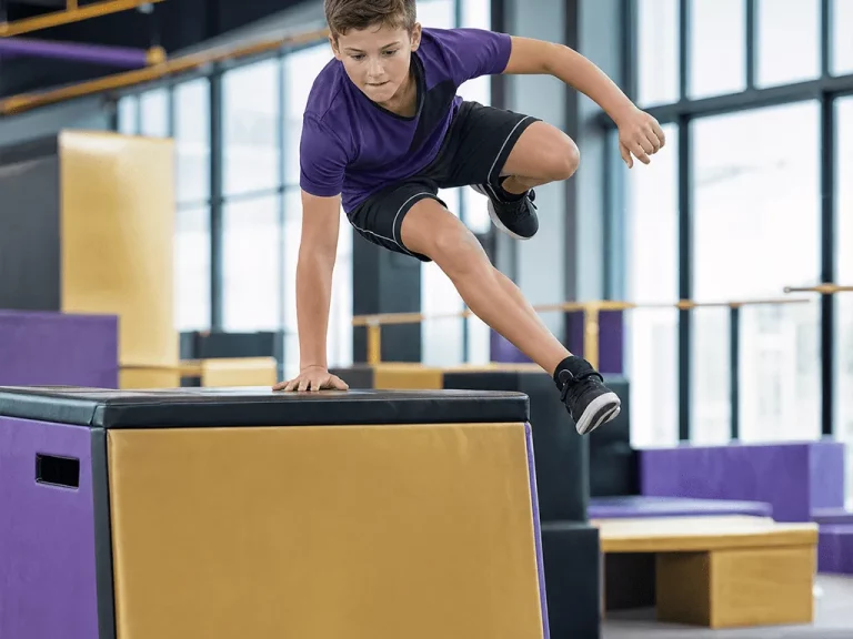 Boy vaulting over a padded box in a parkour class