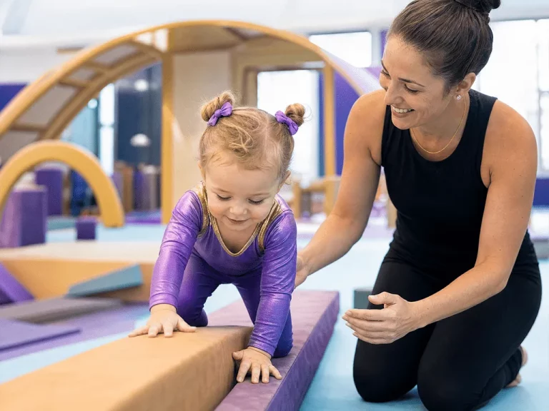 Coach guiding a young girl across a low balance beam