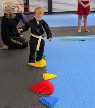 Instructor guiding a young student across stepping cones during a taekwondo class
