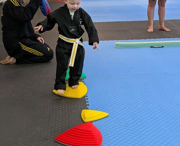 Instructor guiding a young student across stepping cones during a taekwondo class