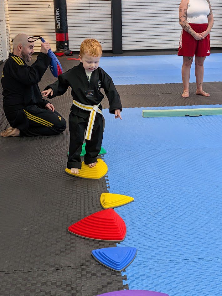 Instructor guiding a young student across stepping cones during a taekwondo class