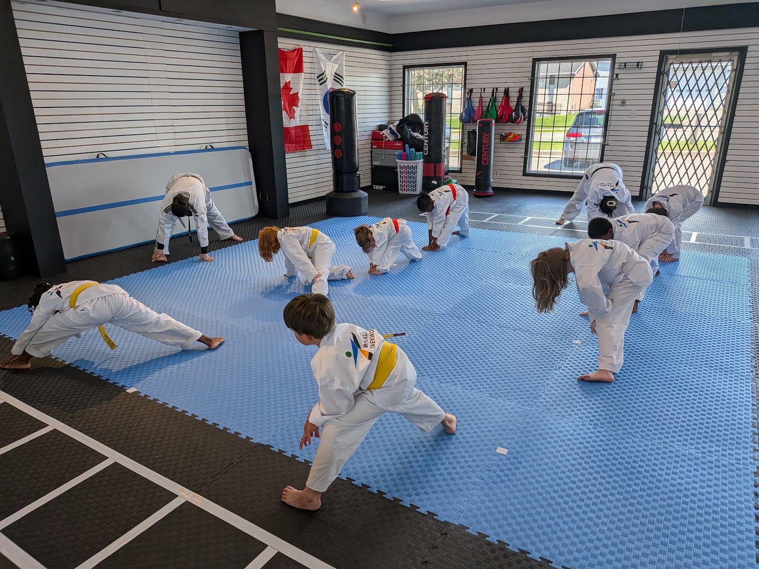 Kids taekwondo class practising stretches on the mats in front of the flags at The RAZ
