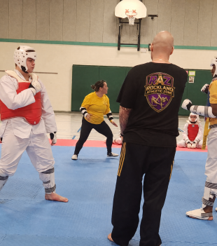 Taekwondo students sparring in protective gear at a school gym