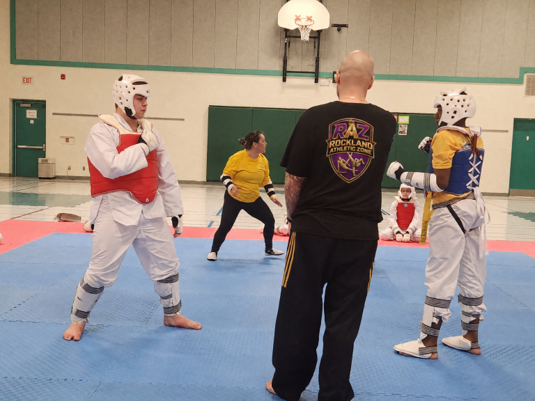 Taekwondo students sparring in protective gear at a school gym
