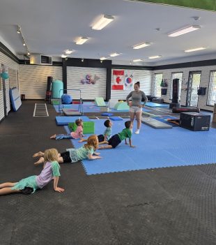 Young gymnasts stretching on the blue floor with their coach at The RAZ