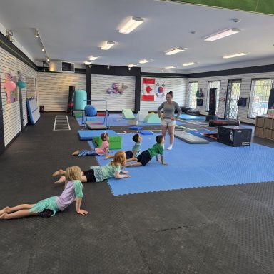 Kids Gymnastics Class with Soft Play in Rockland Young gymnasts stretching on the blue floor with their coach at The RAZ