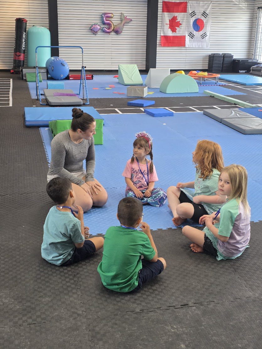 Gymnastics coach talking with a circle of children on the mats at The RAZ