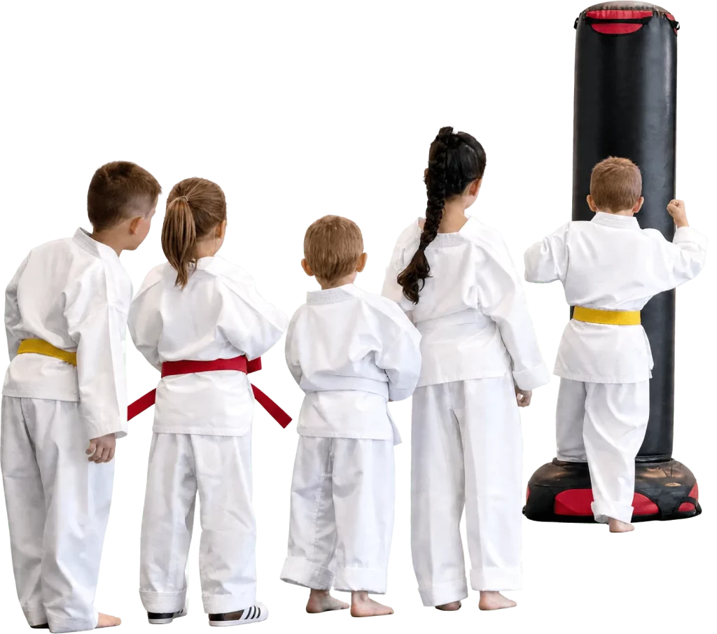 Young taekwondo students in white uniforms lined up beside a punching bag